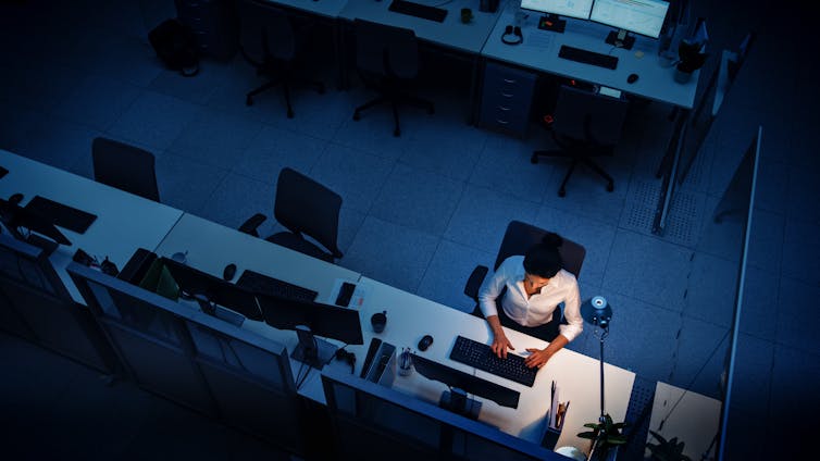 lone woman working at a desk in an office at night.