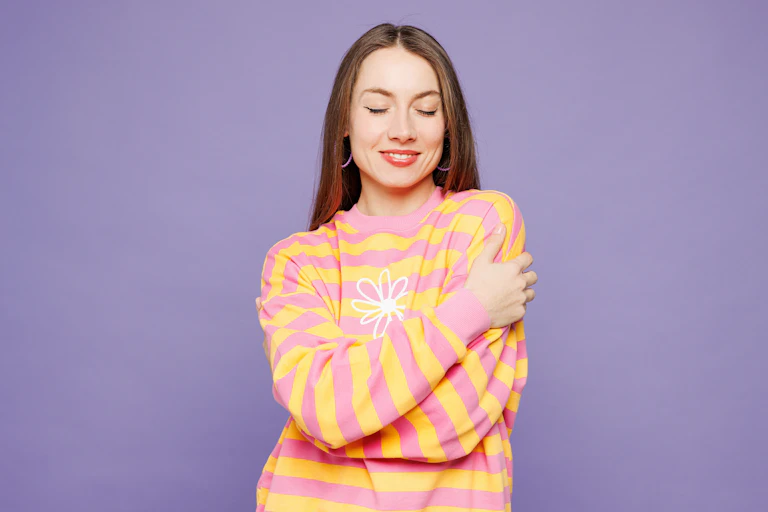 Woman in stripey top giving herself a hug against a purple background.