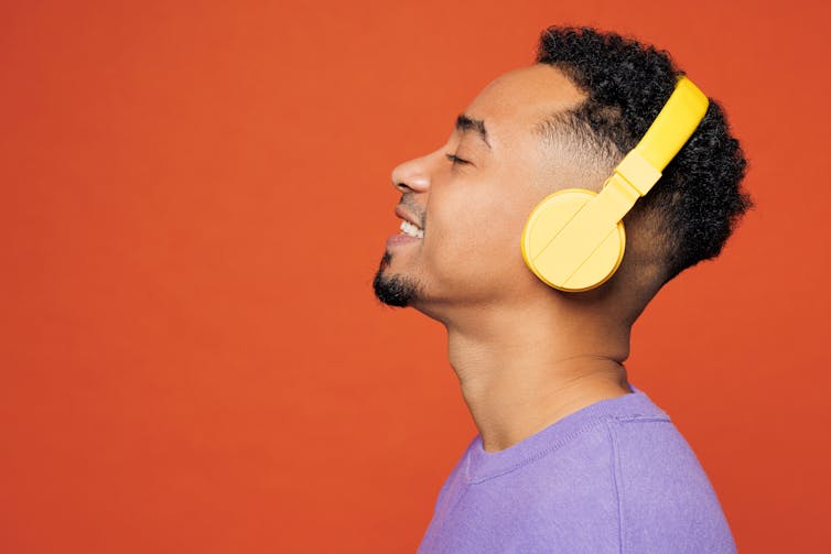 Young man smiling wearing yellow headphones against a red background.