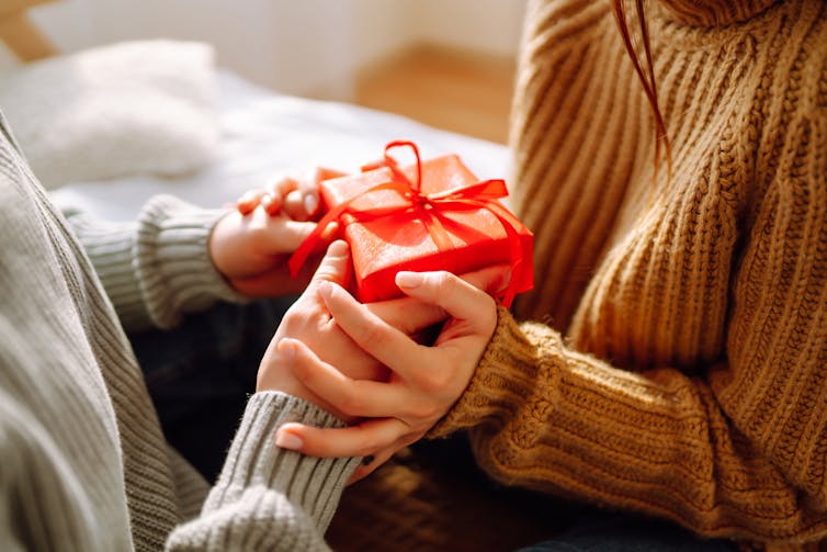 Two people exchanging a red gift box tied with ribbon.