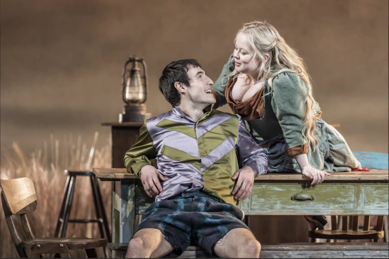 A woman and a man on stage smiling at each other over a table.