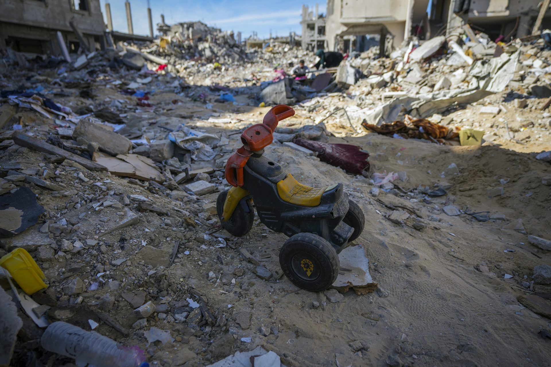 A child's plastic tricycle in the rubble.
