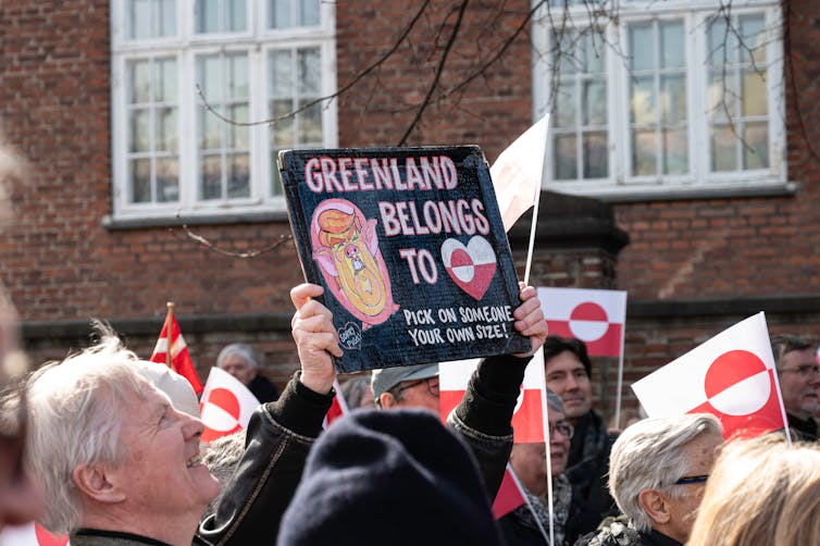 Anti-trump protesters hold placards displaying the Greenlandic flag.