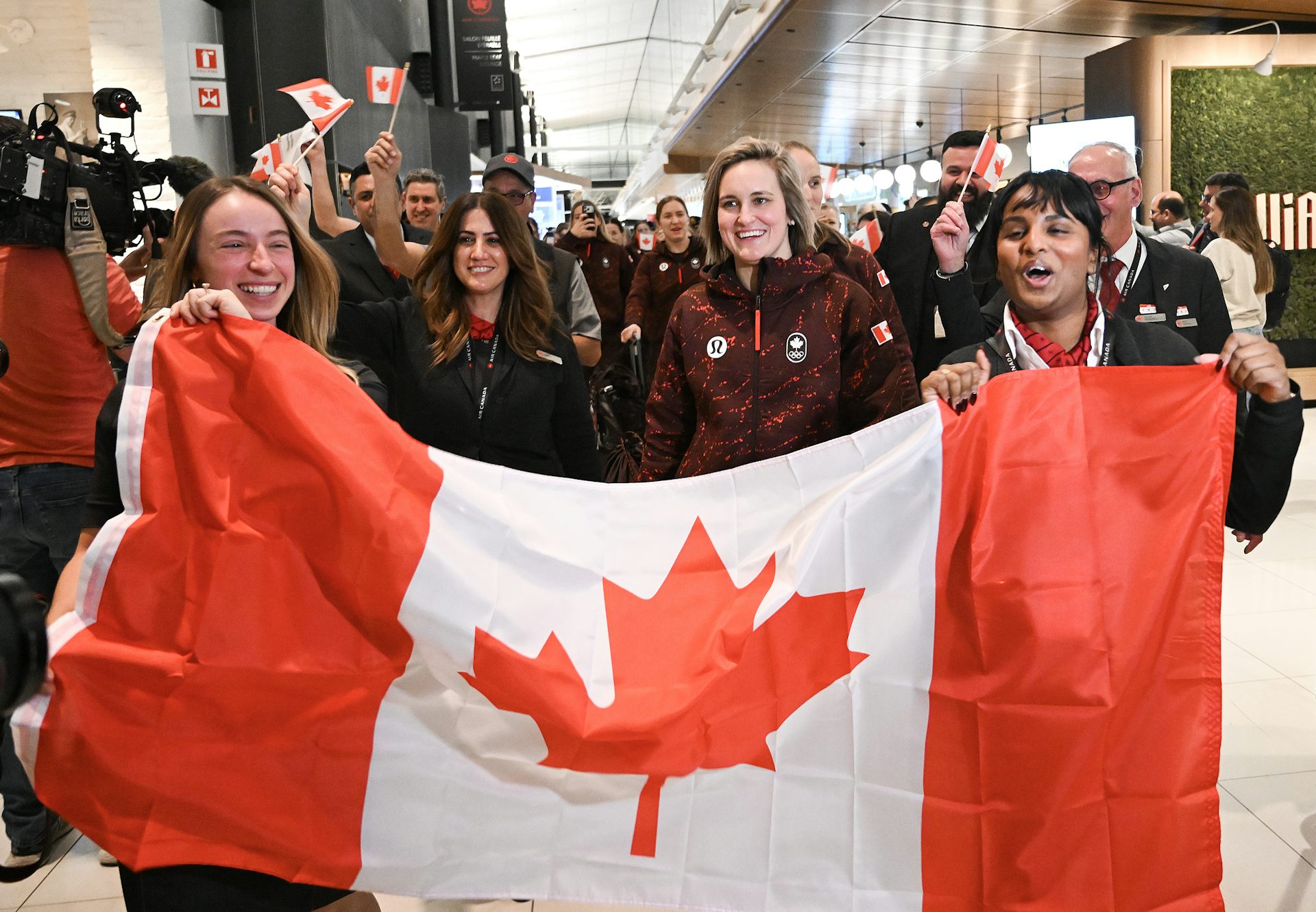 Un groupe de personnes défile en agitant des drapeaux canadiens et en brandissant un grand drapeau comme bannière.
