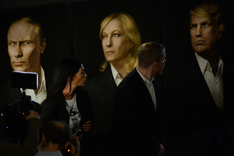 trois portraits (Poutine, Marine Le Pen et Trump) et des personnes qui les regardent.
