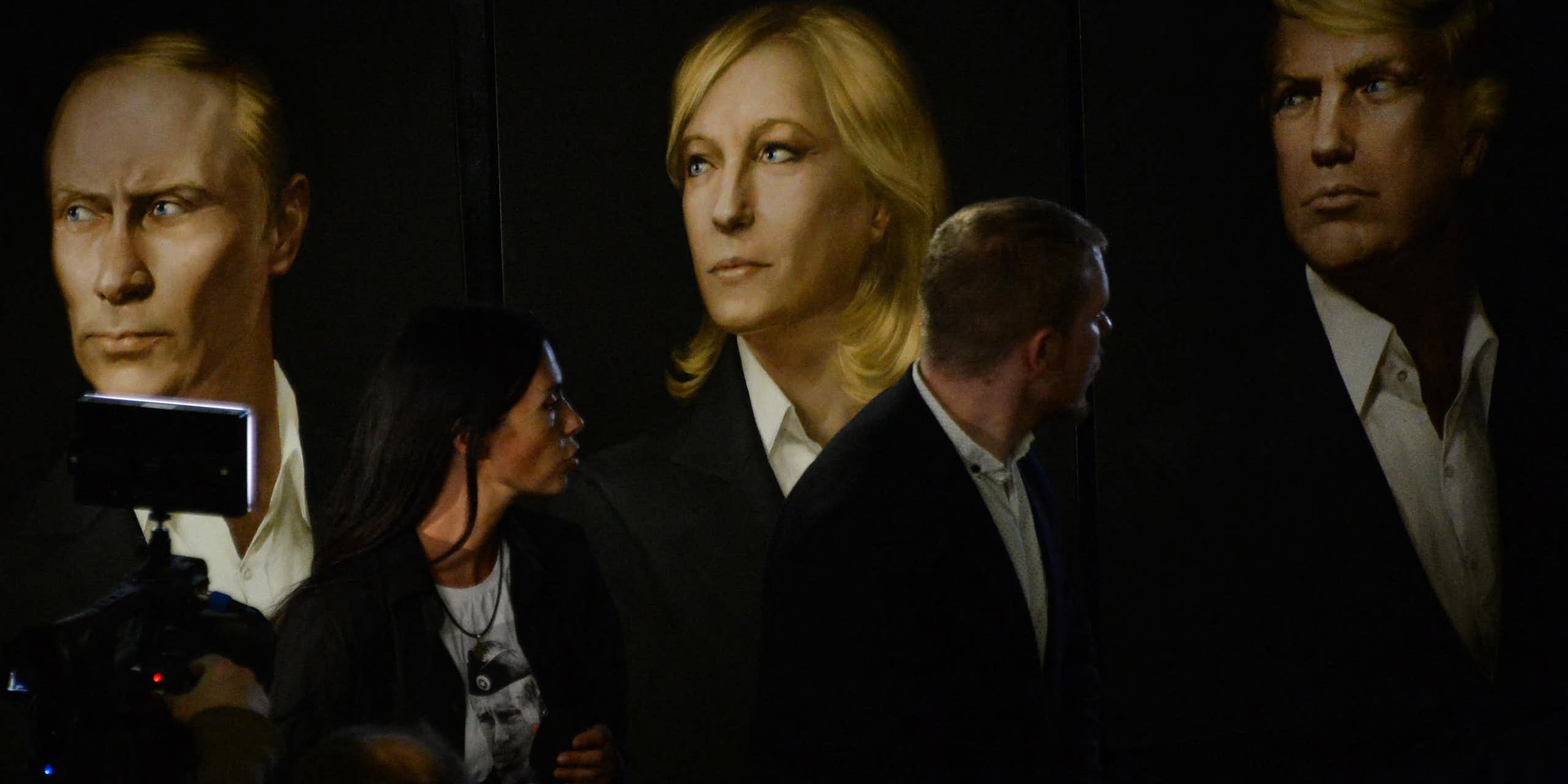 trois portraits (Poutine, Marine Le Pen et Trump) et des personnes qui les regardent.