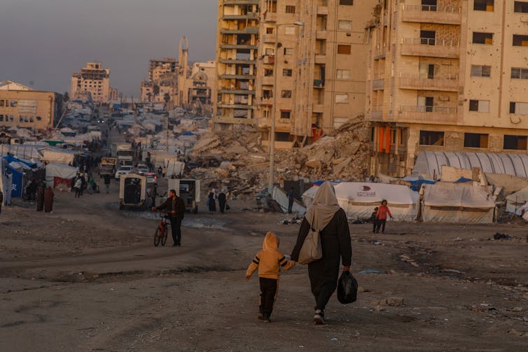 A Palestinian woman and her child walk among destroyed buildings in Gaza City.