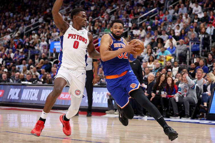 Two professional basketball players battle for the ball. One is wearing a white Detroit Pistons jersey.