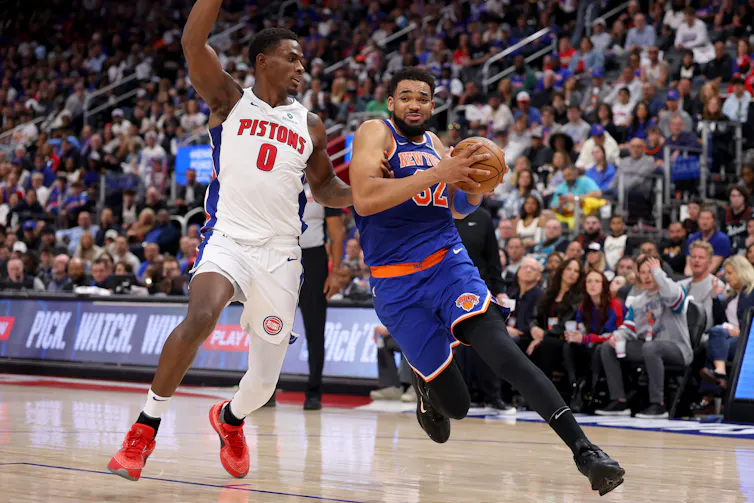 Two professional basketball players battle for the ball. One is wearing a white Detroit Pistons jersey.