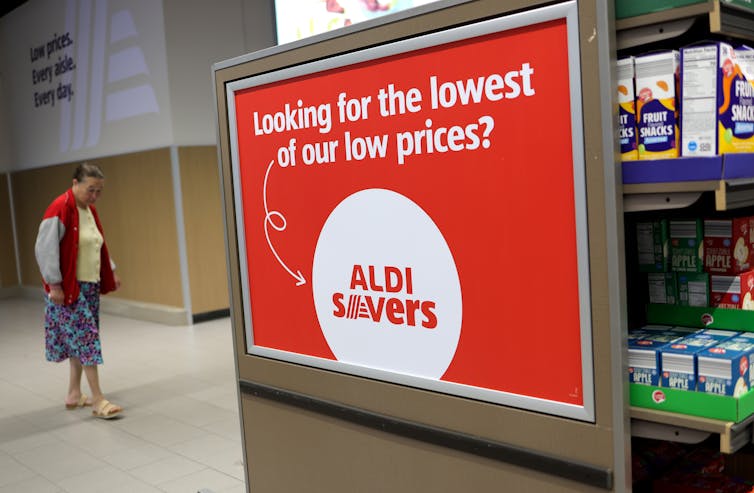 Una mujer se encuentra cerca de un cartel de una tienda de comestibles que dice: