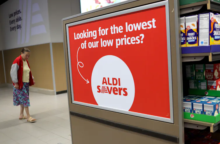A woman stands near a grocery store sign that reads: 'Looking for the lowest of our low Prices? Aldi Savers'
