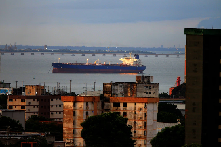 Un barco azul, grande, en las aguas de un lago con un puente de fondo y edificios viejos en primer plano