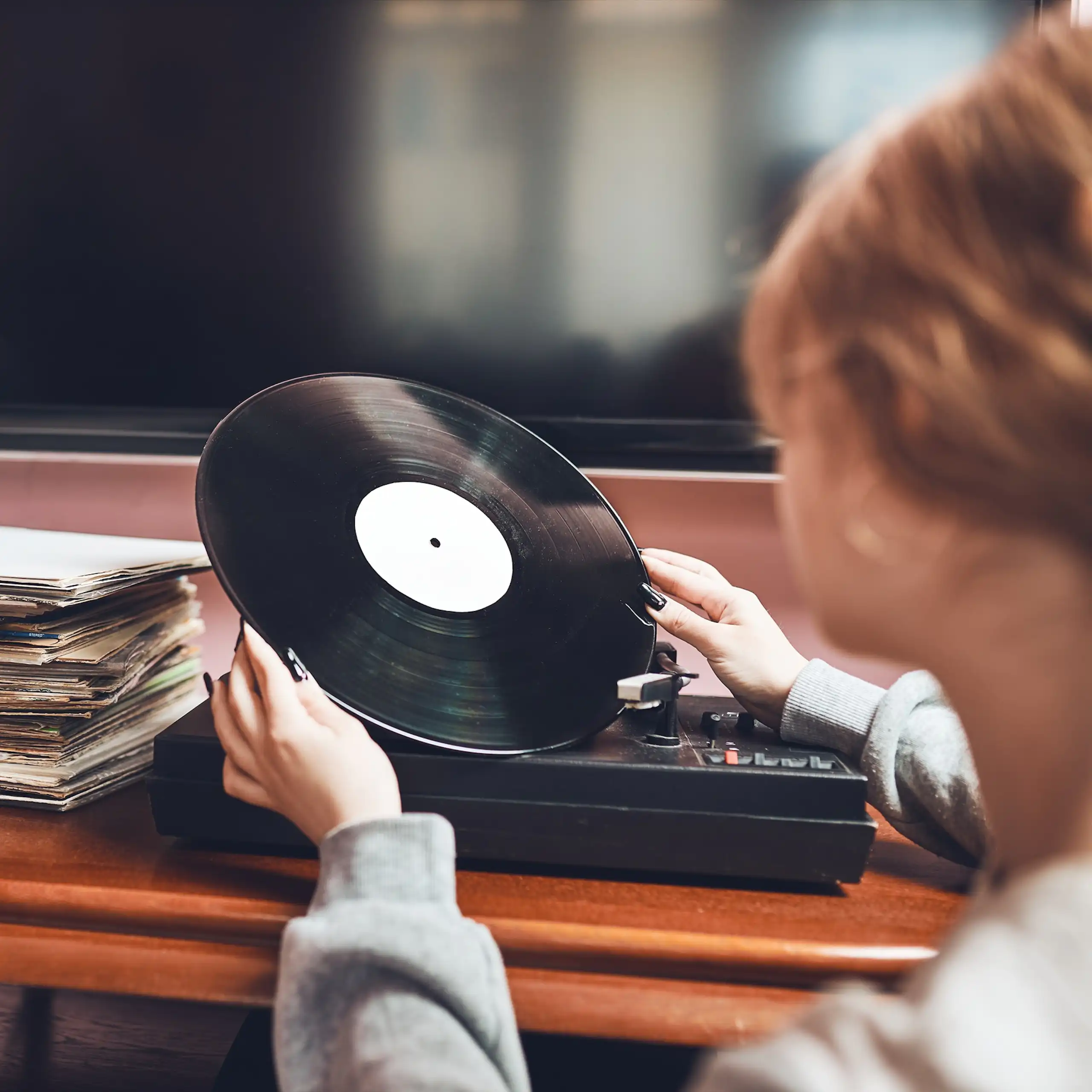 Una mujer observa un disco de vinilo frente a un tocadiscos.