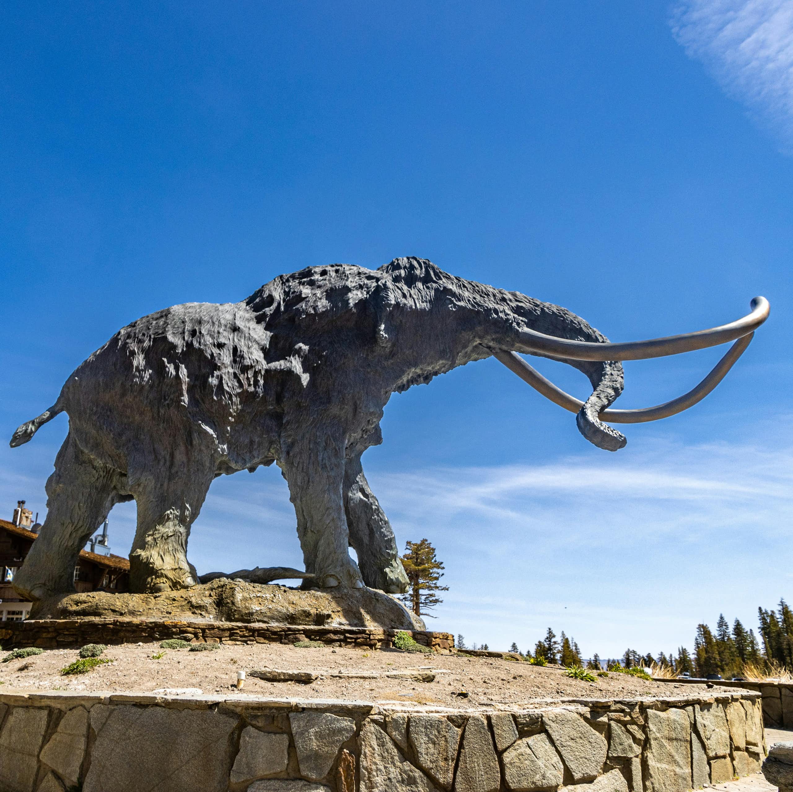 Estátua de um mamute lanoso contra um céu azul.