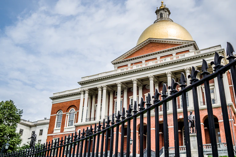 A large elegant building with a gold dome and white pillars, set behind an elegant black iron fence.
