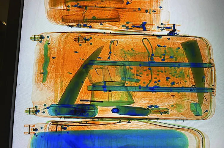 An image with artificial coloring shows the contents of a suitcase, including two long pointed solid objects.