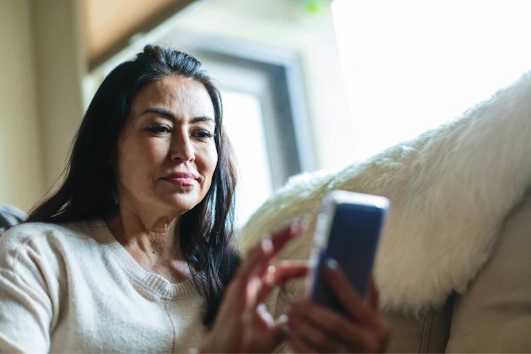 Woman looks at her phone while sitting on her sofa
