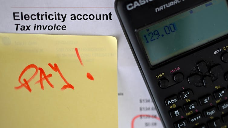 A photo illustration of an electricity bill with a calculator and a sticky note