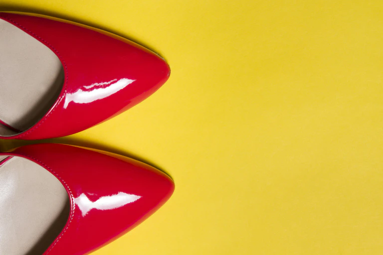 Pair of pointy red, patent leather shoes on yellow background