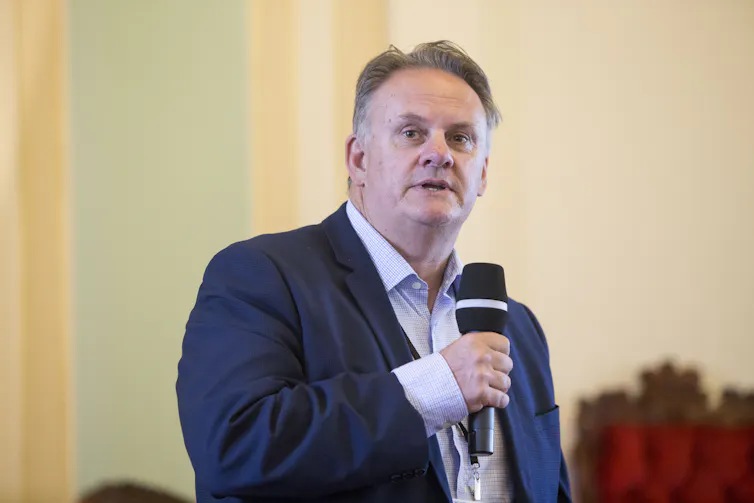 A man in a suit, no tie, with a microphone