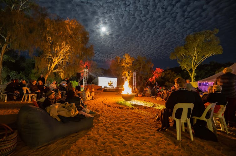 People on chairs in the dark in the desert, listening to a speaker