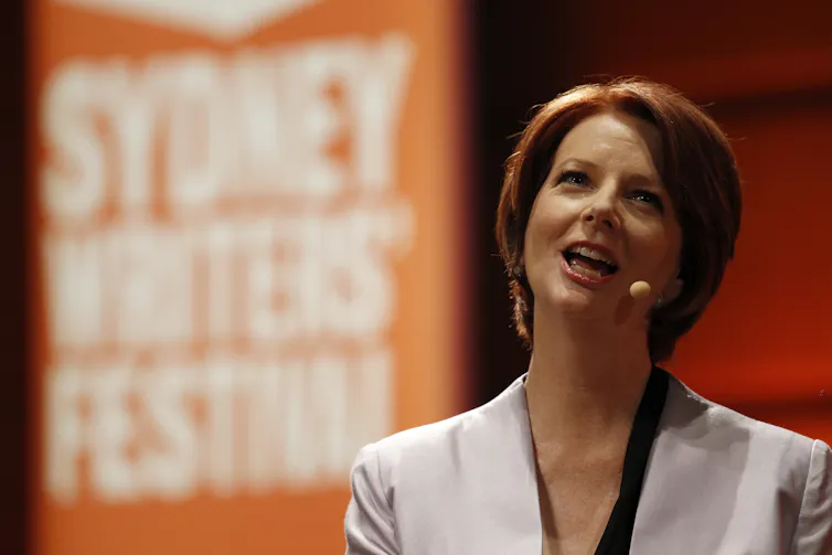 A woman with a red bob and a microphone attached to her, in front of a sign: Sydney Writers Festival