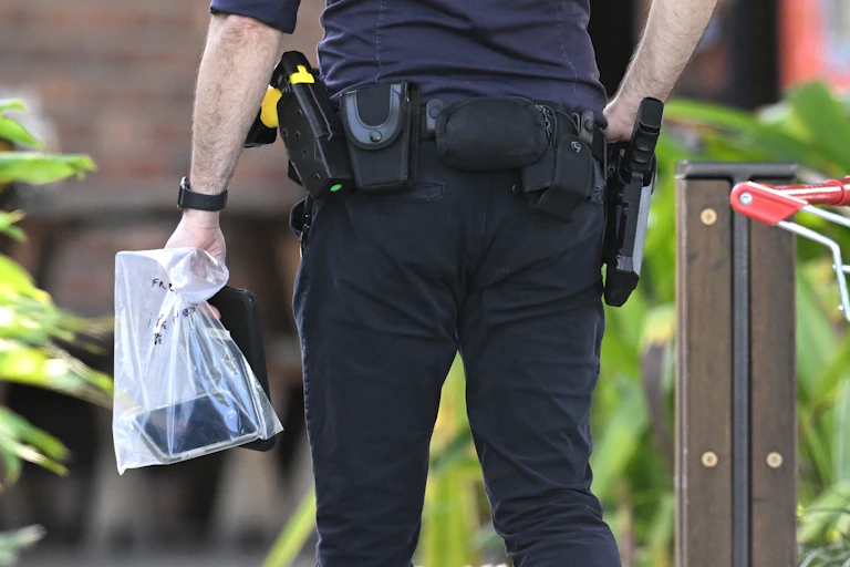 a man's legs and lower torso, as he caries a plastic bag with a phone in it and guns on his holster