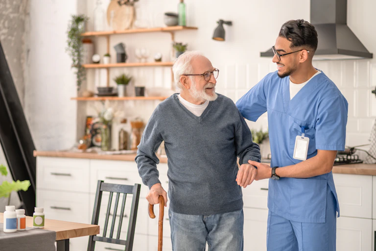 A carer helps an elderly patient to move around his home.