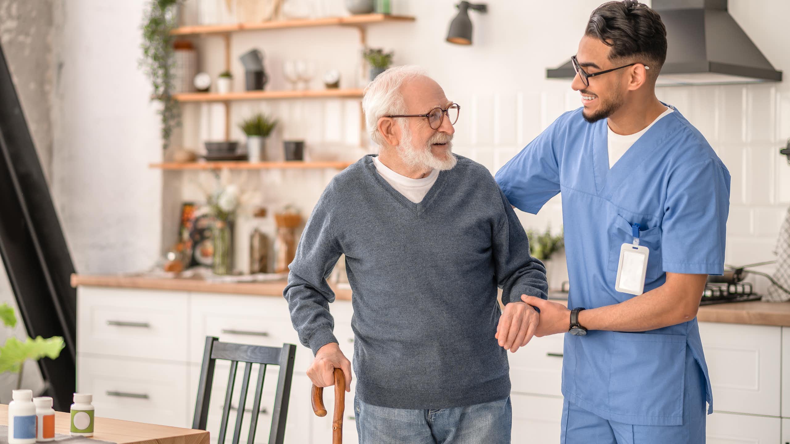 A carer helps an elderly patient to move around his home.