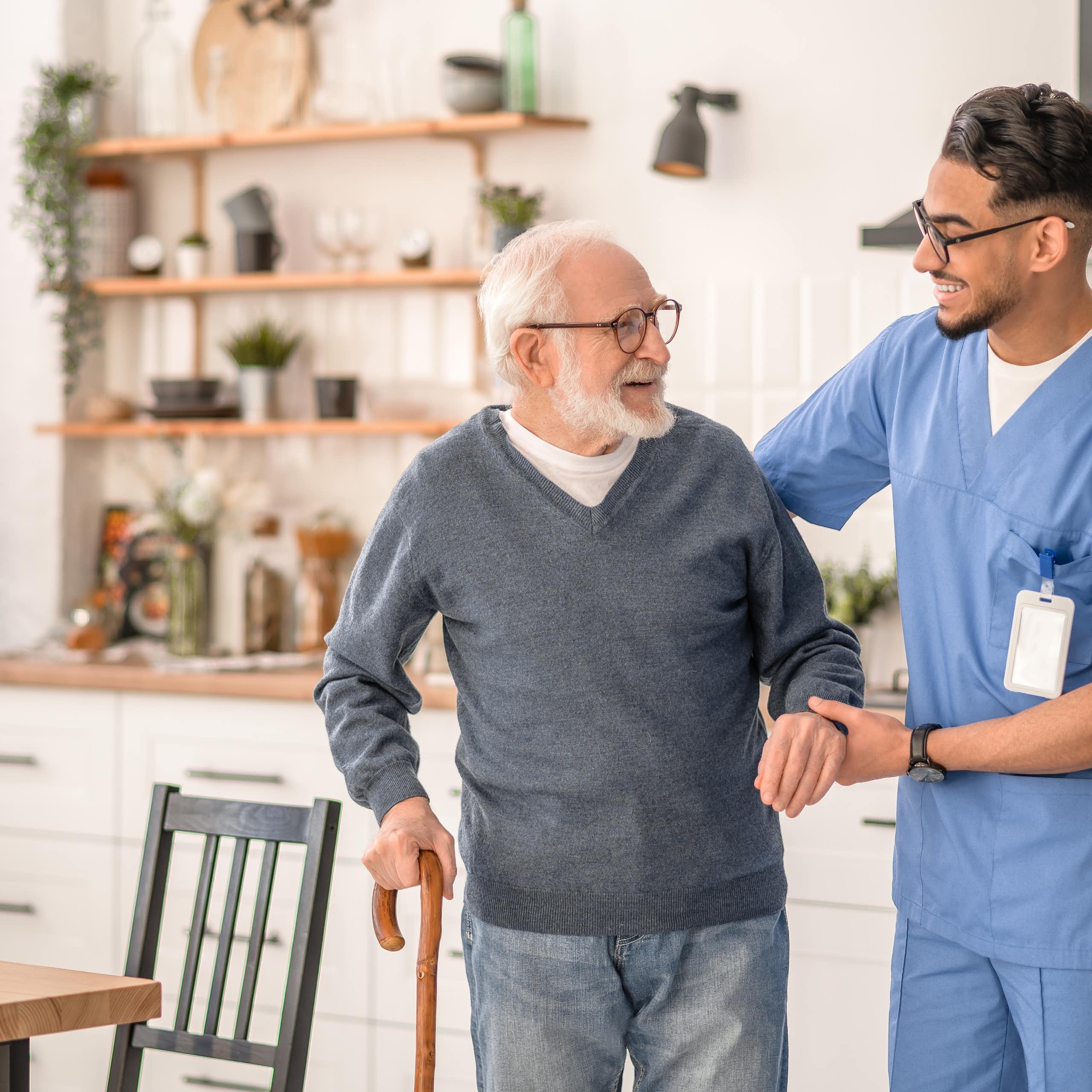 A carer helps an elderly patient to move around his home.