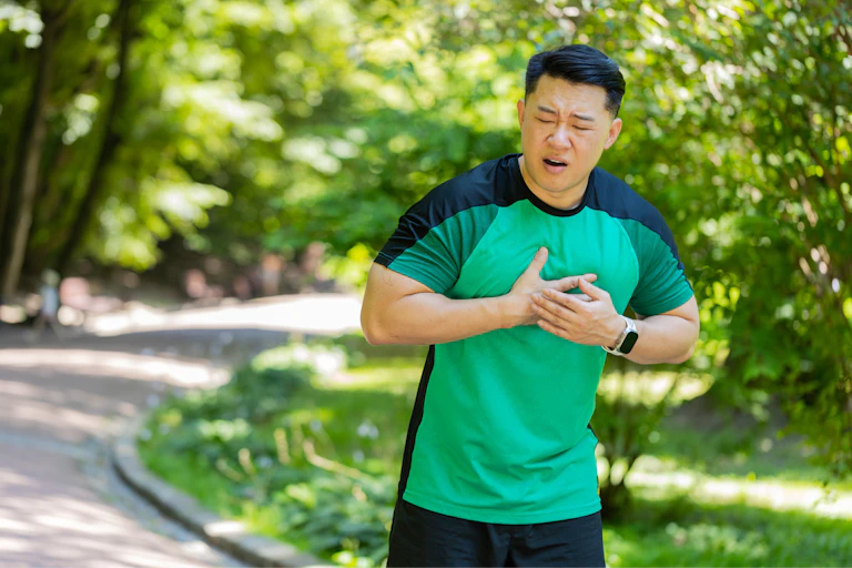 A fit man exercising outdoors holds his chest in pain.