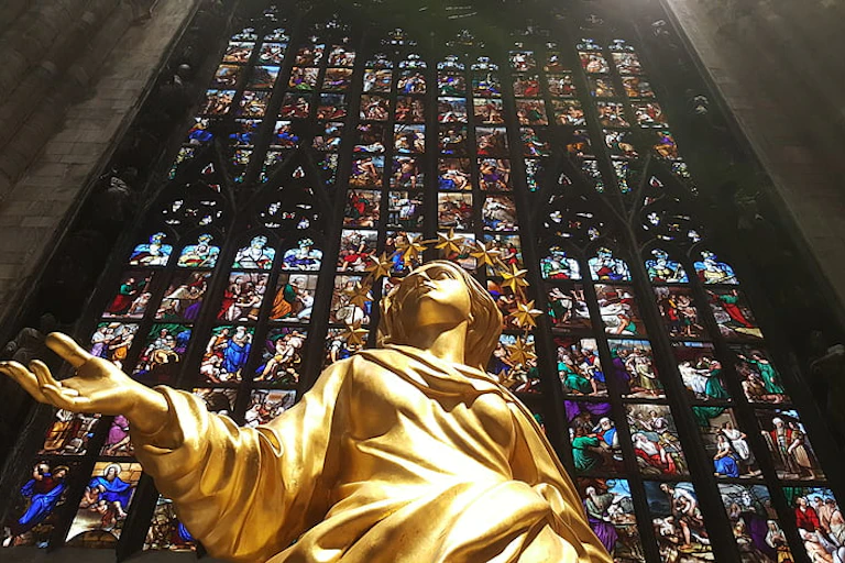 Statue of a woman against a stained glass window inside a church