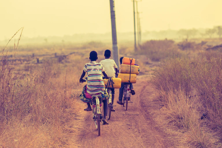 Adolescents on bicycles carry tubs of drinking water on a rural path.