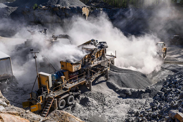 Large pieces of equipment in an open mine, with clouds of dust