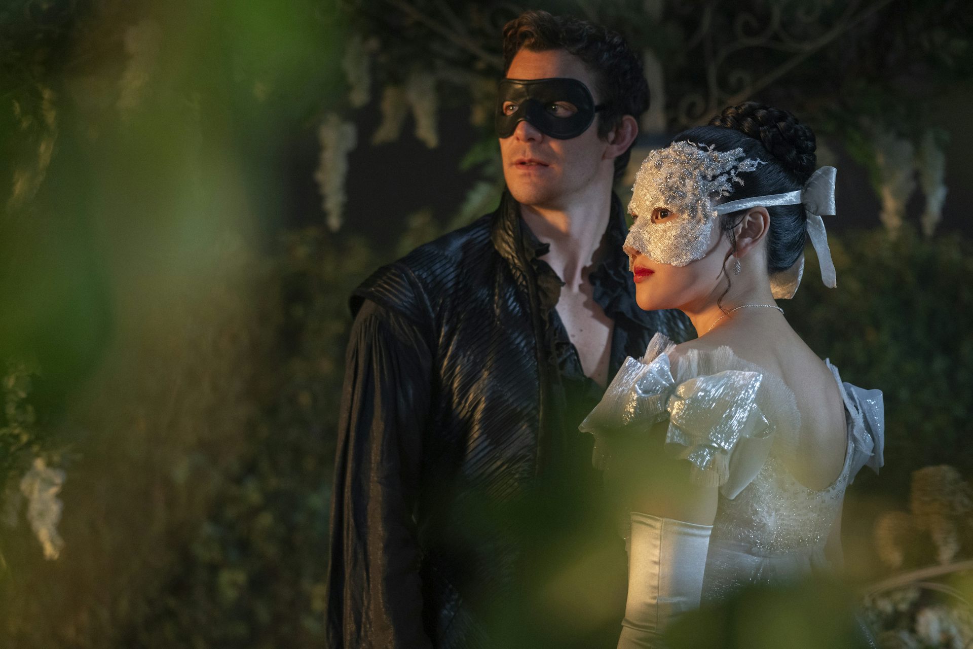 Luke Thompson as Benedict Bridgerton and Yerin Ha as Sophie Baek both wearing masquerade masks