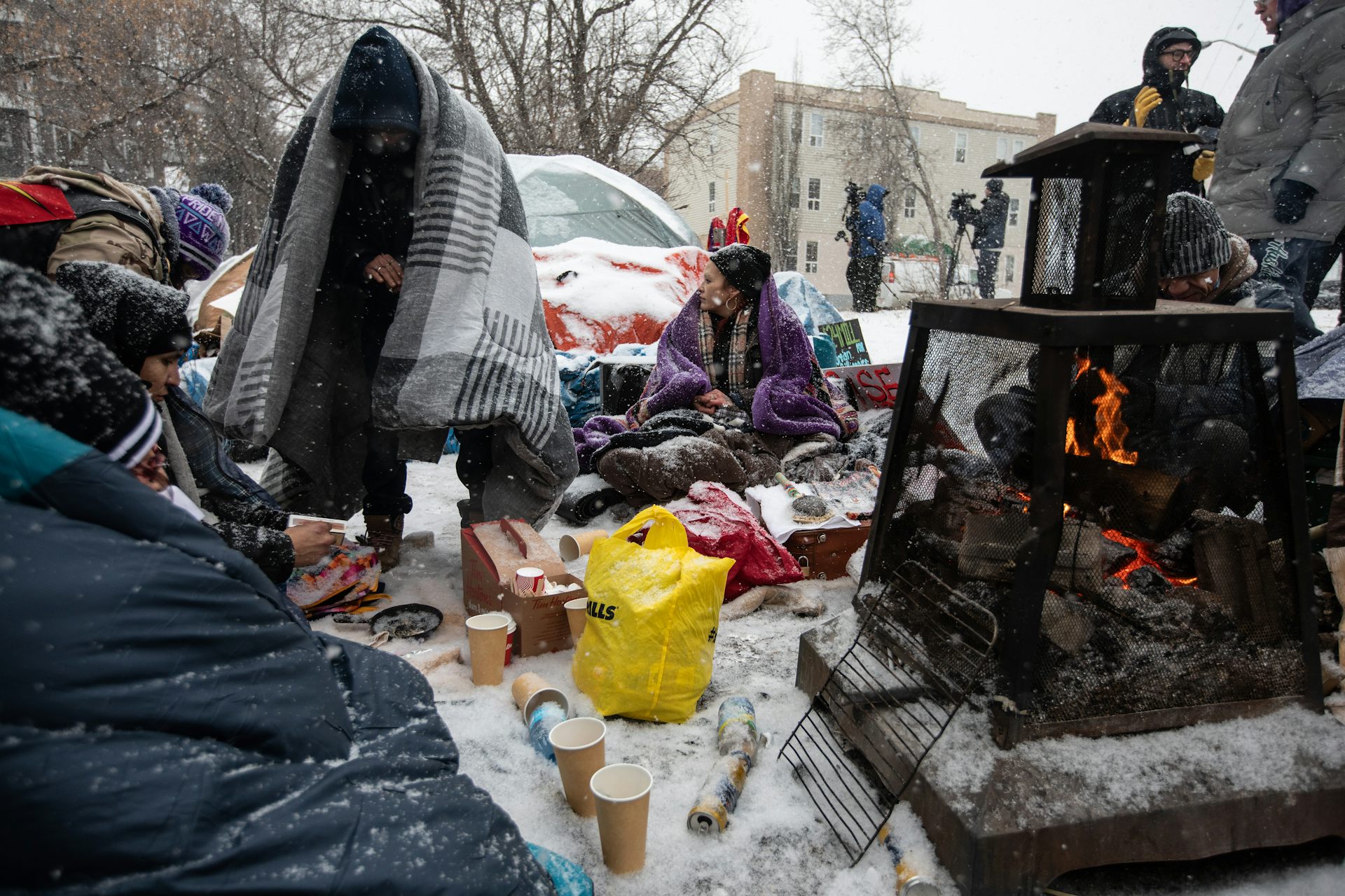 Un grupo de personas abrigándose en invierno en un campamento para personas sin hogar.