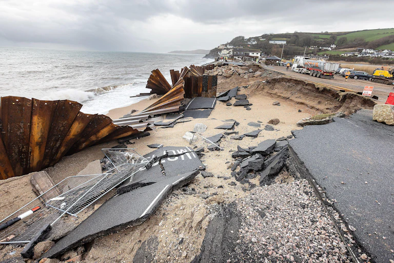 damage coastal road, broken tarmac and metal sea defence crumpled up