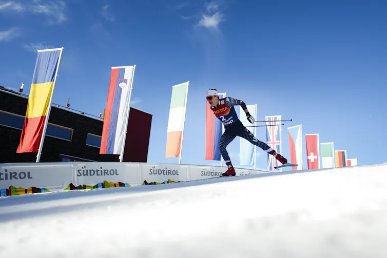 A male skier races down a slick track with flags flying along the wall beside him