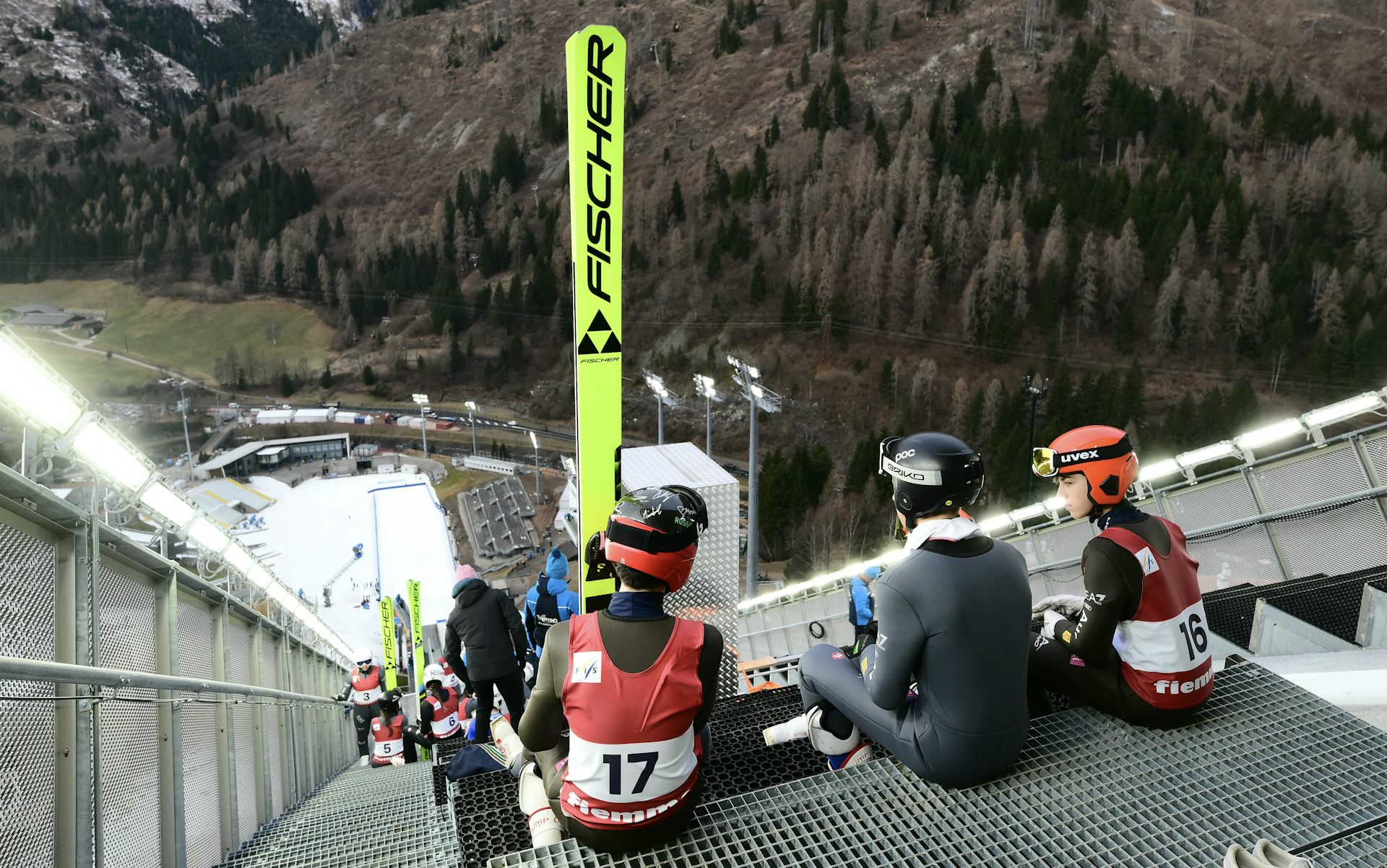 Tres esquiadores están sentados encima del salto de esquí. Su vista muestra lo seco que está el suelo sin nieve alrededor de la zona de salto.
