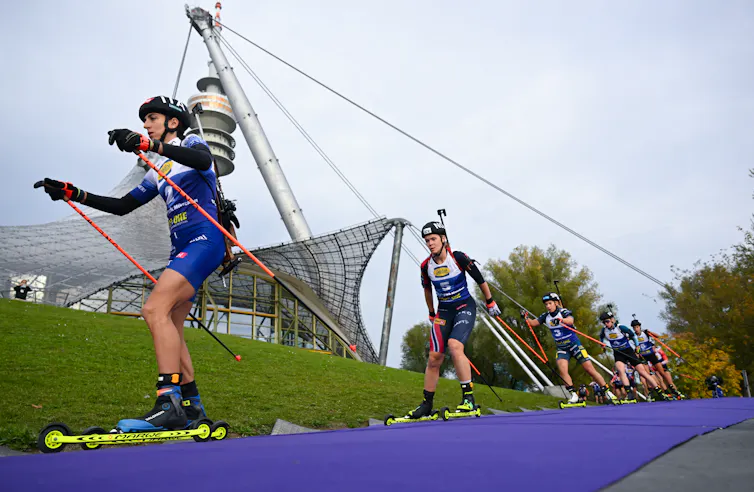 Athletes race on short skis on wheels.