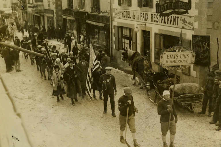 A procession down a street with someone carrying an American flag.