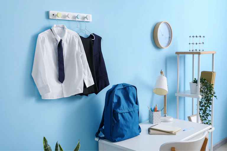 school uniform hanging on pegsa on blue wall, school bag on desk