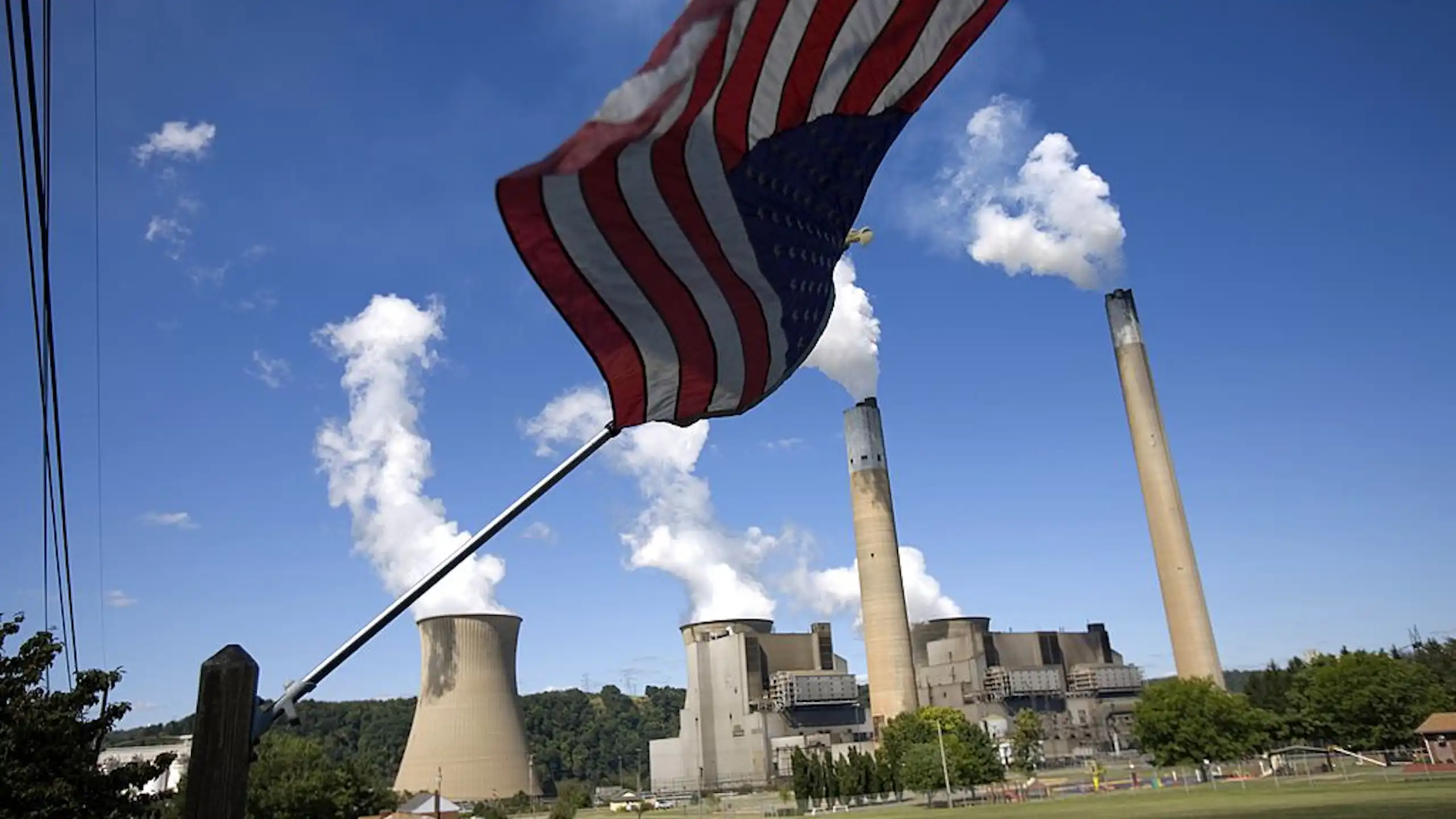 Smoke puffs out of a power plant with an American flag in the foreground of the photo.