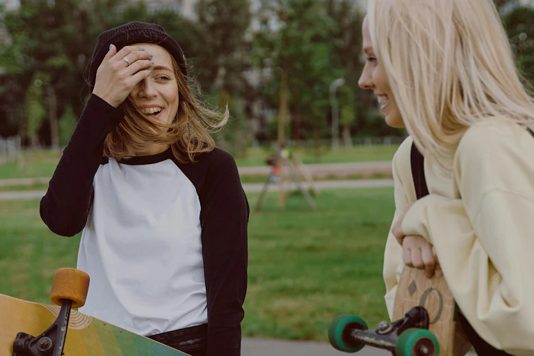 Two teens standing and laughing, one of whom is holding a skateboard.