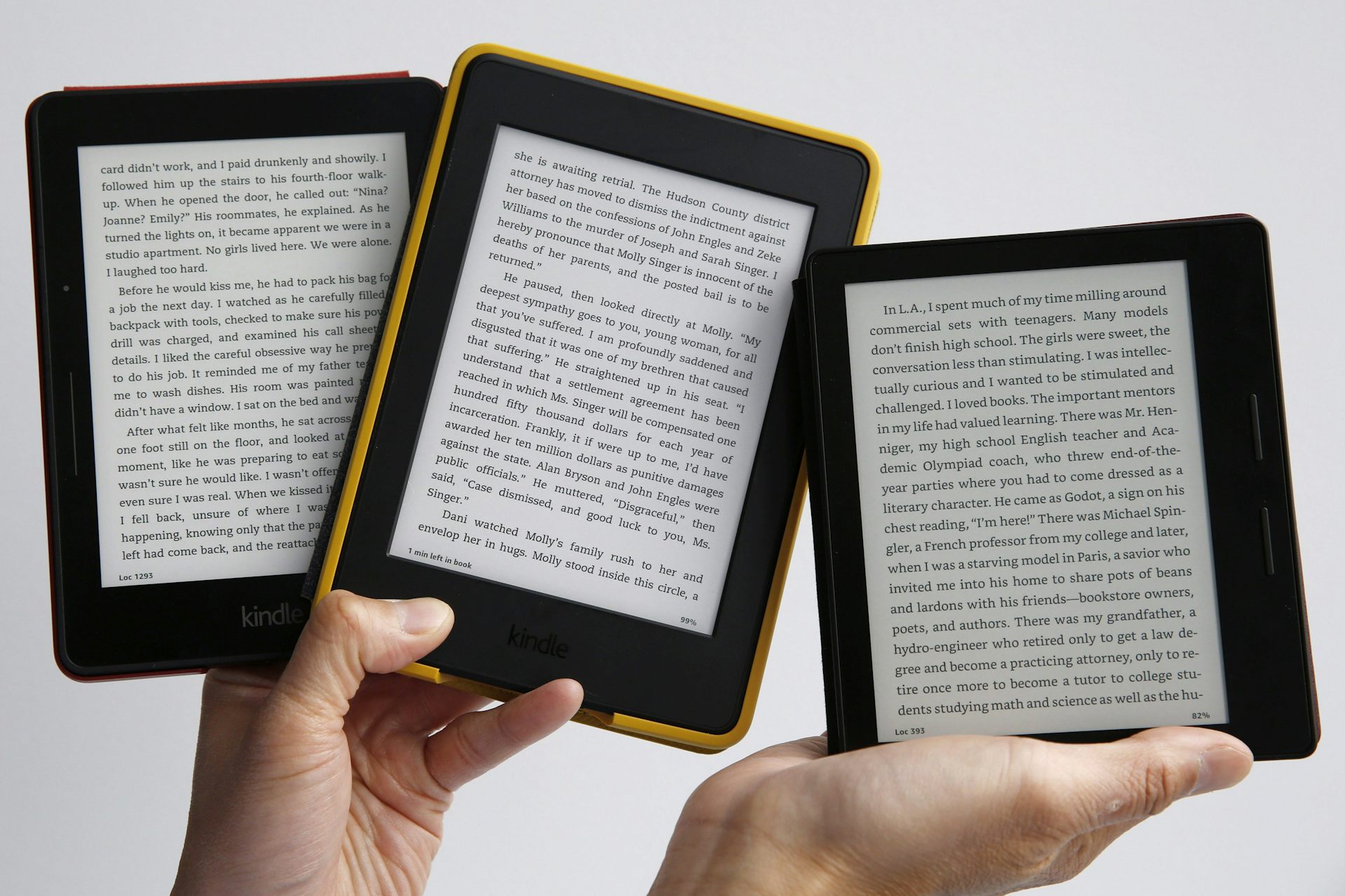 A pair of hands holding up three e-book readers
