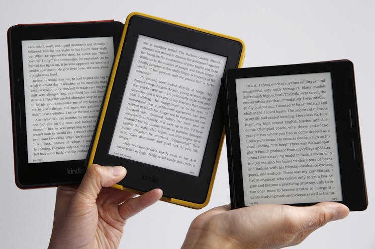 A pair of hands holding up three e-book readers