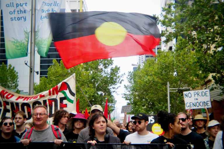 An Aboriginal flag flies in the air above a crowd of protesters holding signs