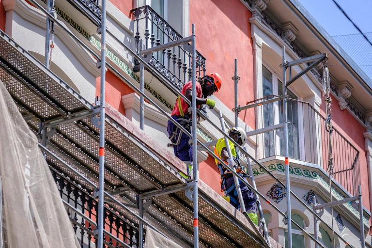 Two black men standing on scaffolding working on the facade of a building
