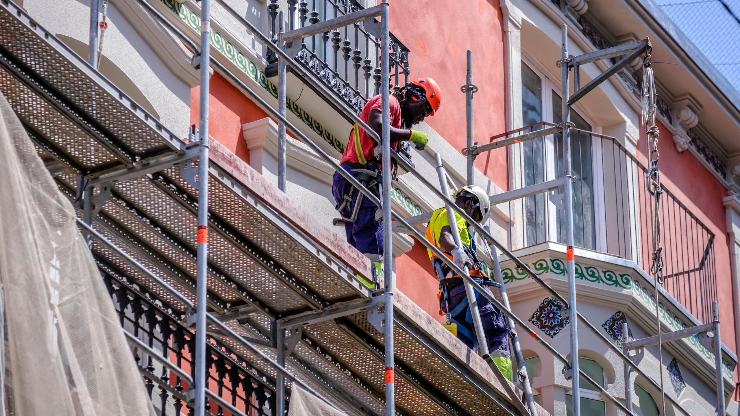 Two black men standing on scaffolding working on the facade of a building