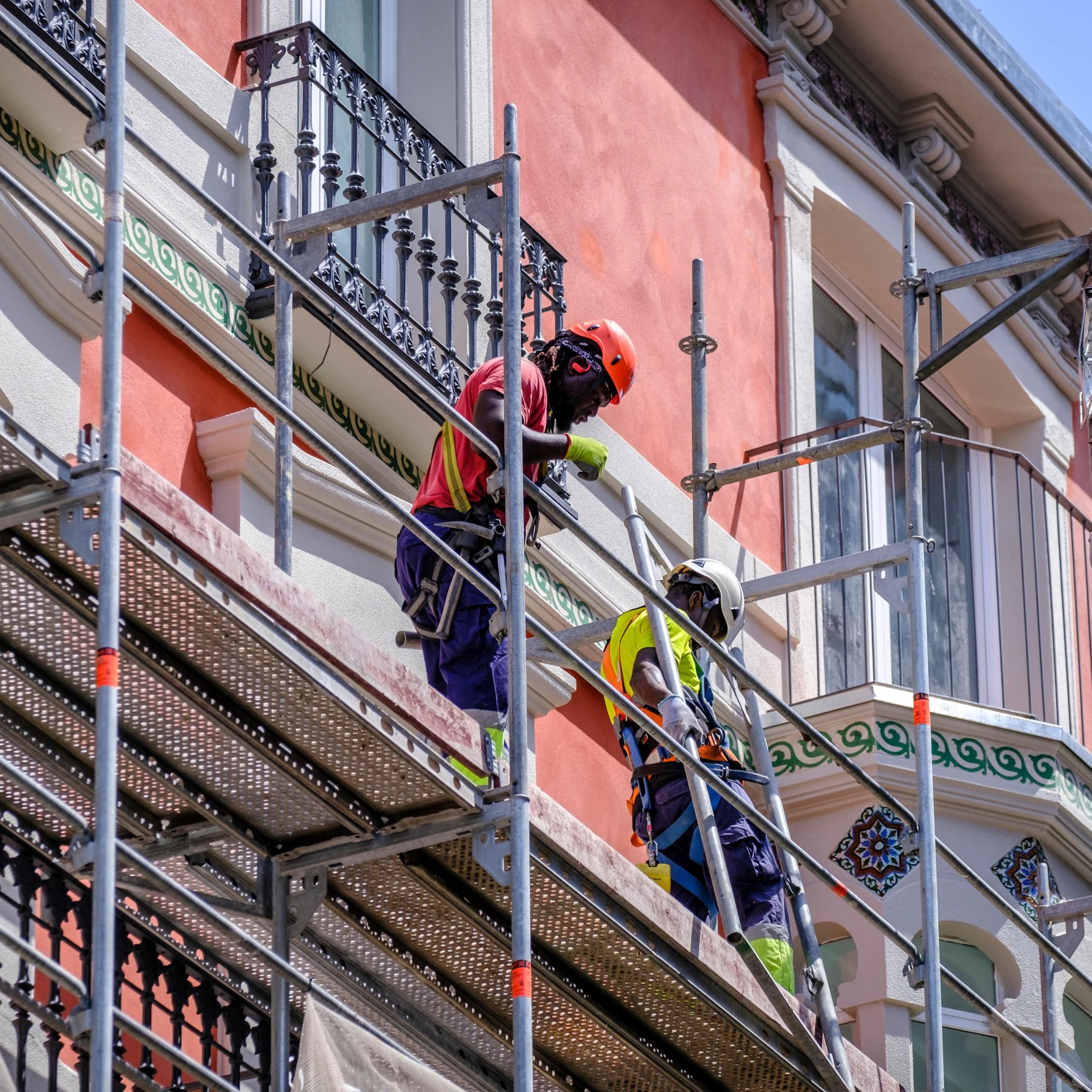 Two black men standing on scaffolding working on the facade of a building